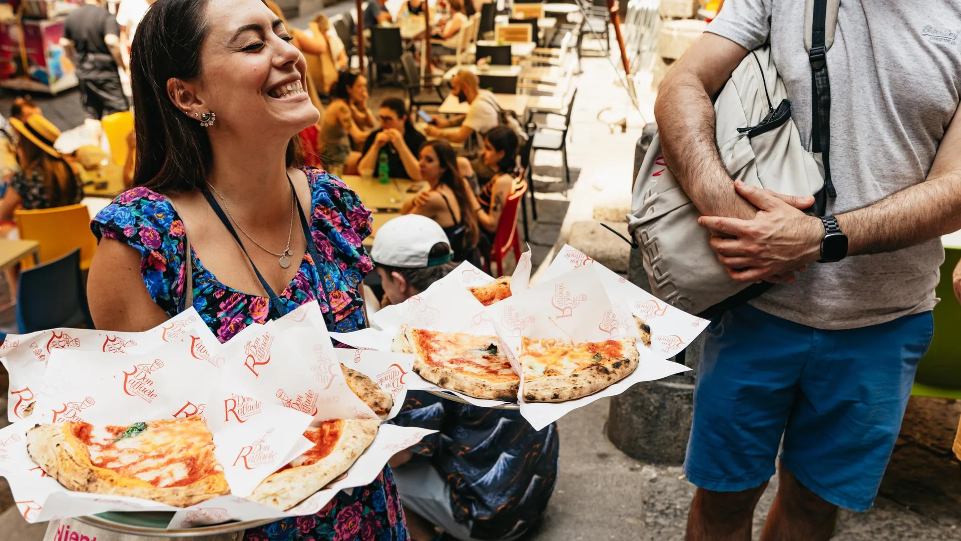 A guide handing out fried pizza in paper to a smiling group in a busy old-town street, from the Naples food tour listing