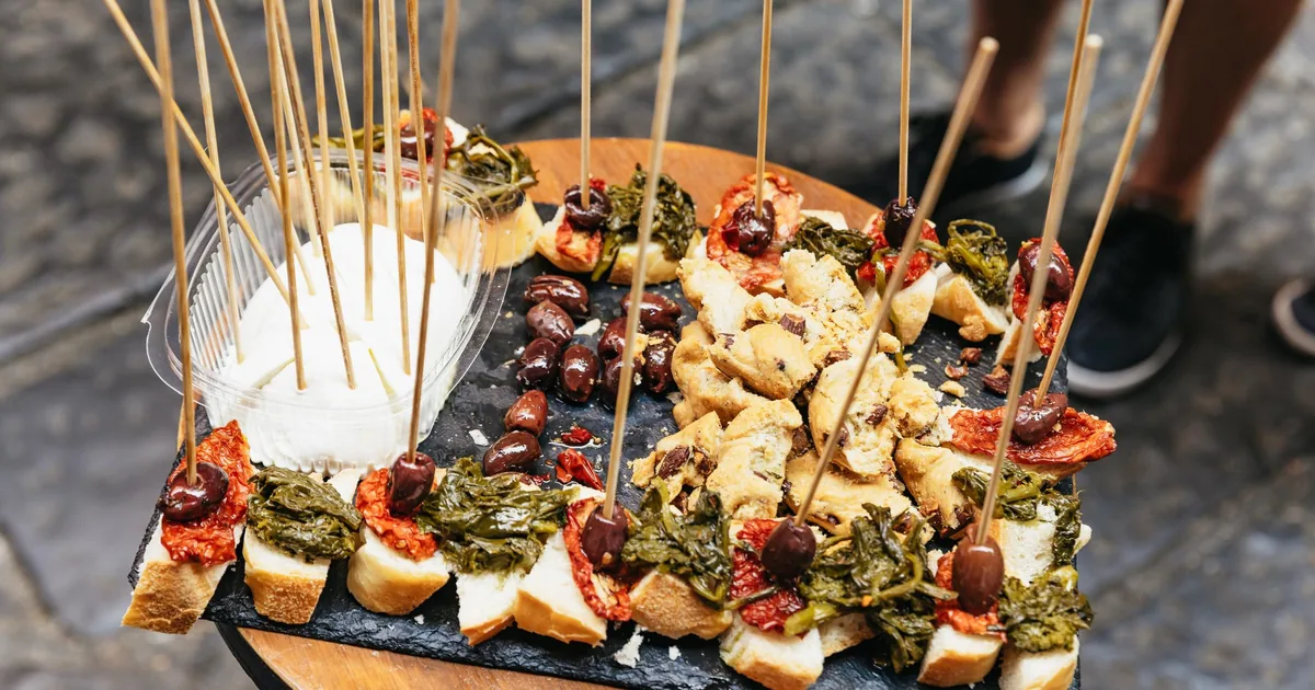 A wooden board of Neapolitan antipasti on skewers, with mozzarella, salami and vegetables, on a food tour stop