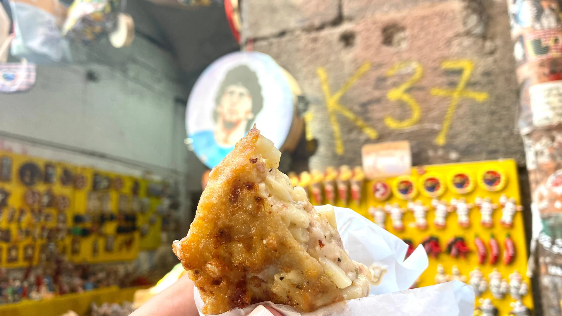 A folded fried pizza held up in front of a street shrine to Maradona, from the old city street food tour listing