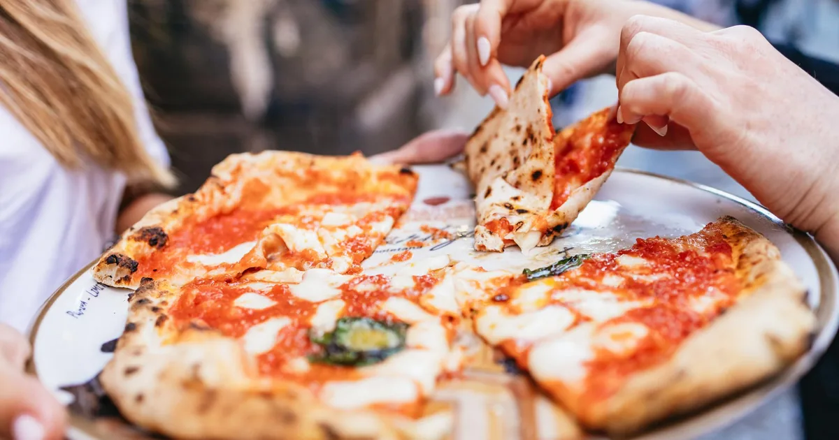 Slices of Neapolitan pizza with tomato, mozzarella and basil on a plate, being shared on a food tour