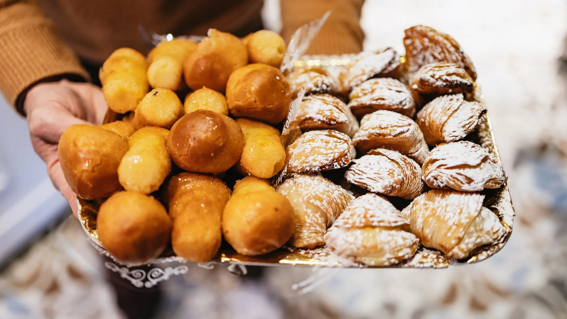 A tray of glossy rum babà and shell-shaped sfogliatelle held out on a Naples street food tour, from the street food walking tour listing