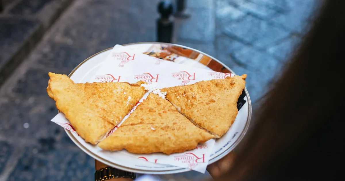 A plate of golden pizza fritta cut into quarters, held over the paving stones of an old Naples street