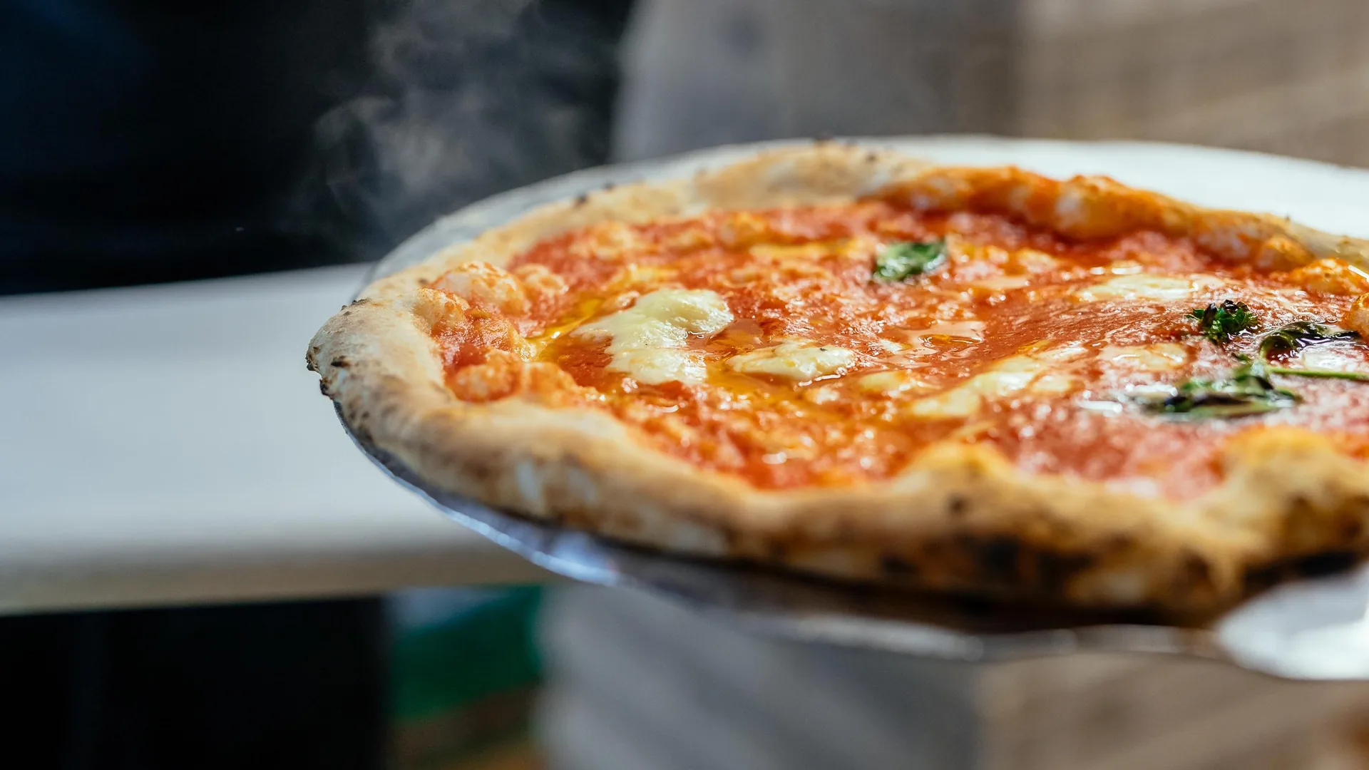A Neapolitan pizza with tomato and mozzarella held out on a peel, from the private food tour listing